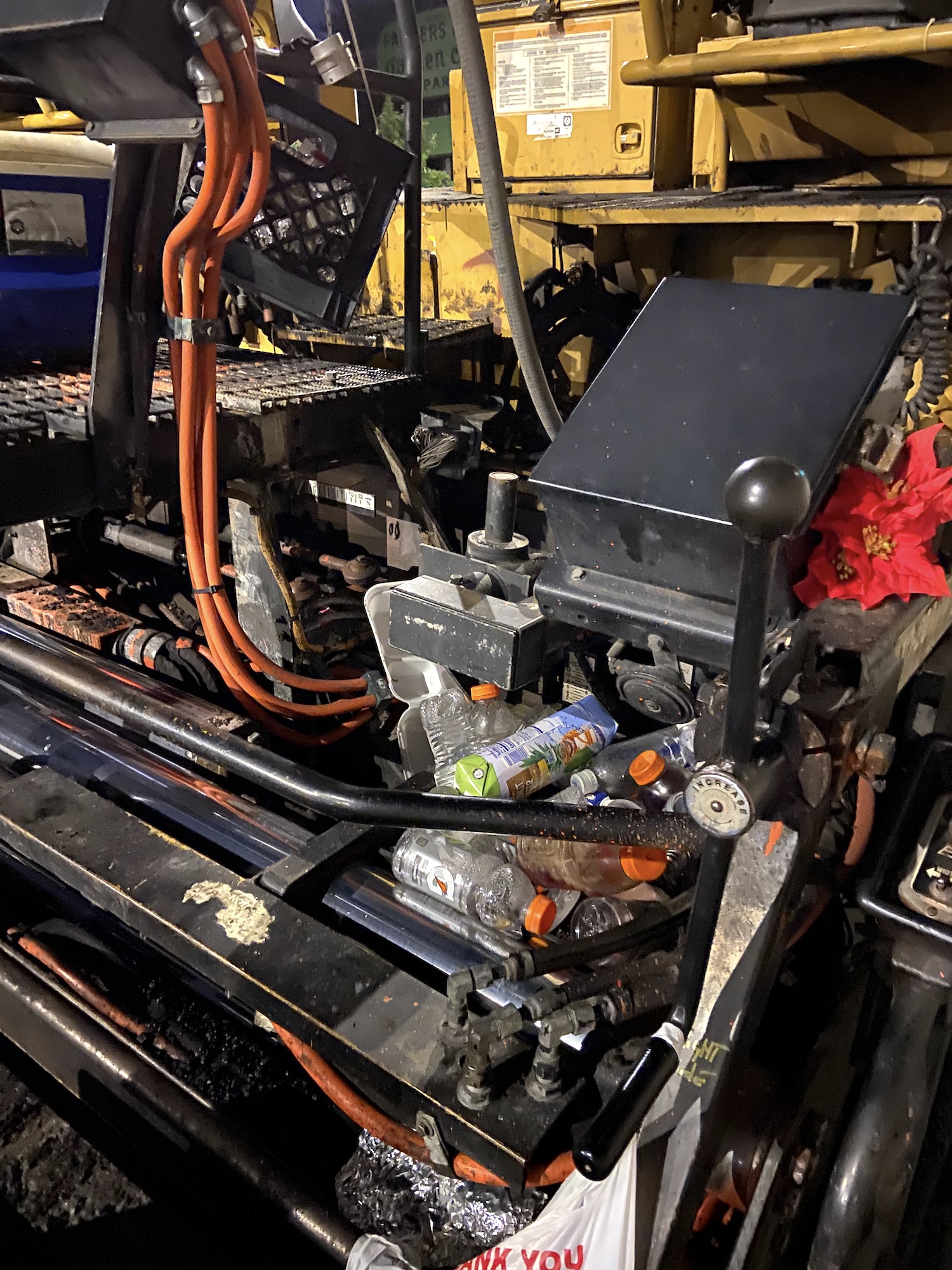 A pile of empty Gatorade bottles beneath the seat of an asphalt paving machine.